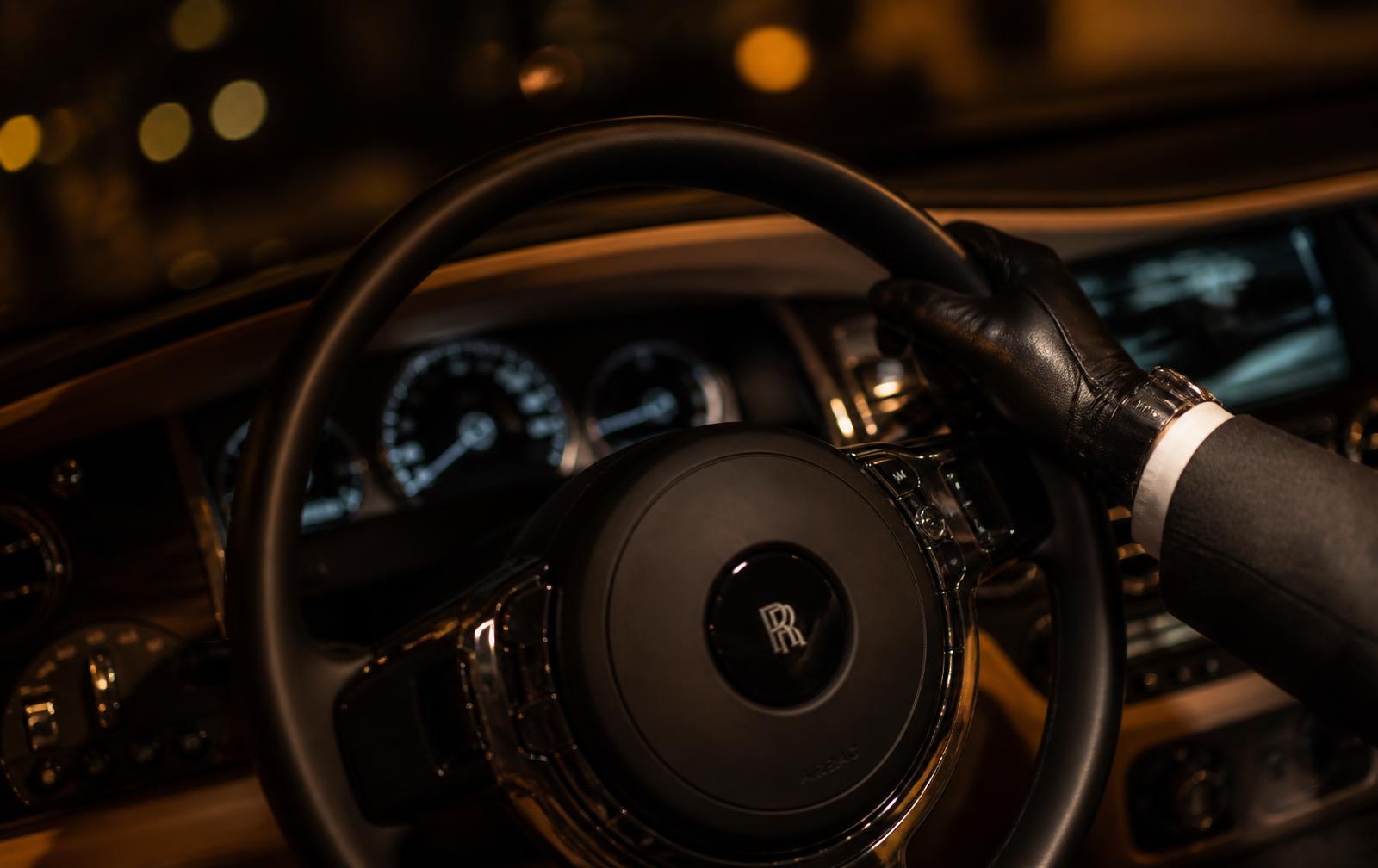 Close-up of a chauffeur's hand on the steering wheel of a luxury car at night